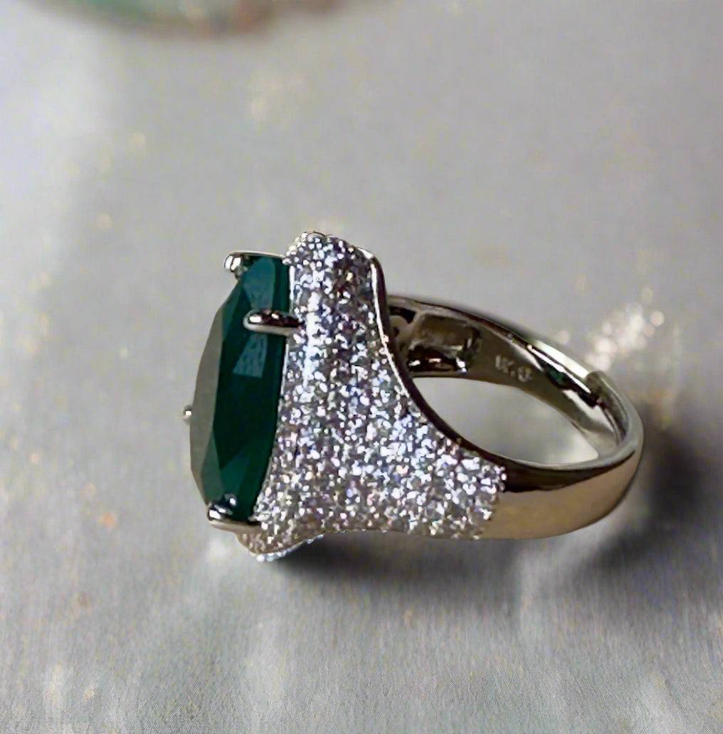 Ring with a green gemstone and diamond-studded band on a textured surface