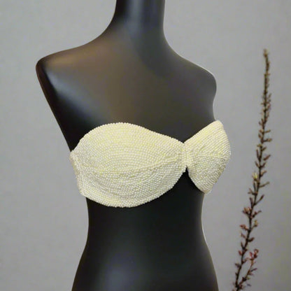 Mannequin wearing a light-colored beaded bikini top against a neutral background