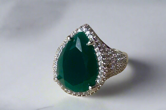 Ring with a green teardrop-shaped gemstone and silver border on a beige surface.