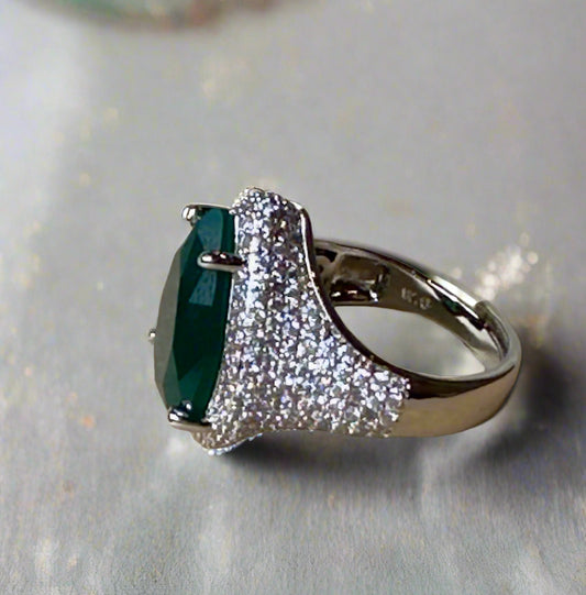 Ring with a green gemstone and diamond-studded band on a textured surface